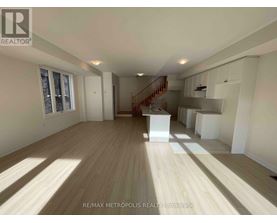 A spacious room with wooden flooring and a staircase leading to the upper level.