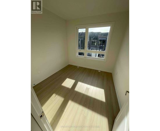 A room with wooden flooring and a window showing a view of houses.