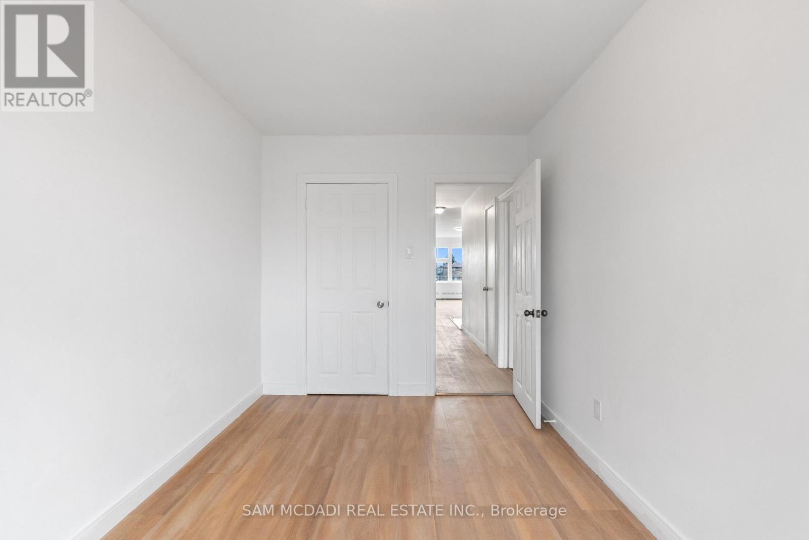 A white hallway with wood floors and doors on either side.