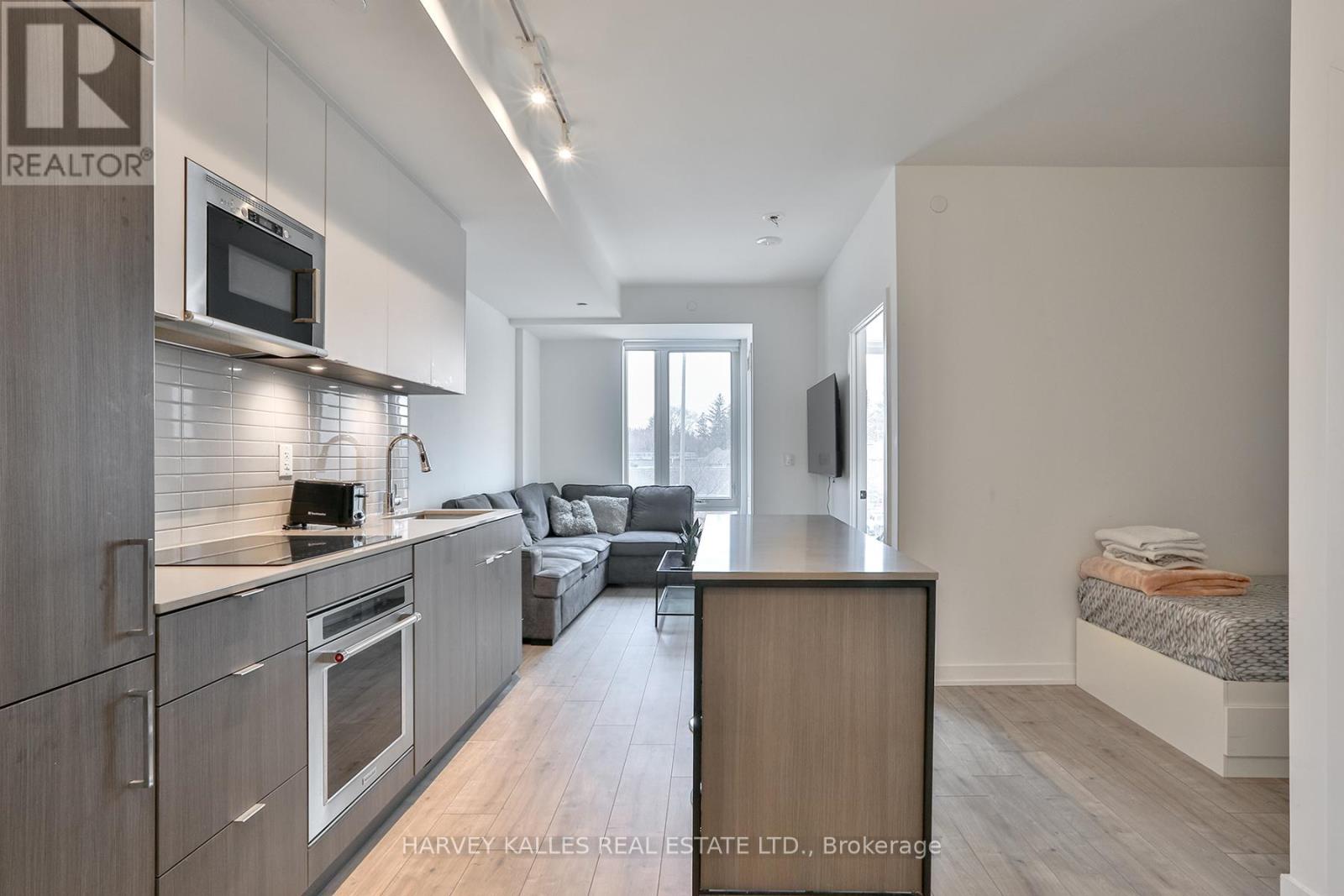 A modern kitchen with a microwave above the oven and a dining area with a couch and a TV.