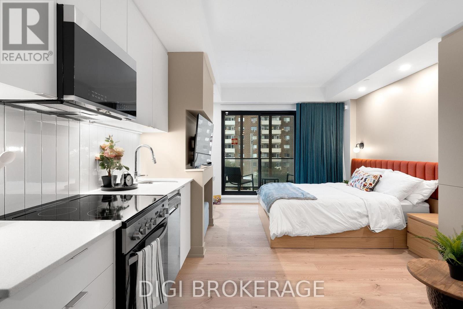 A modern kitchen with a large island and a bedroom with a large bed in the background.