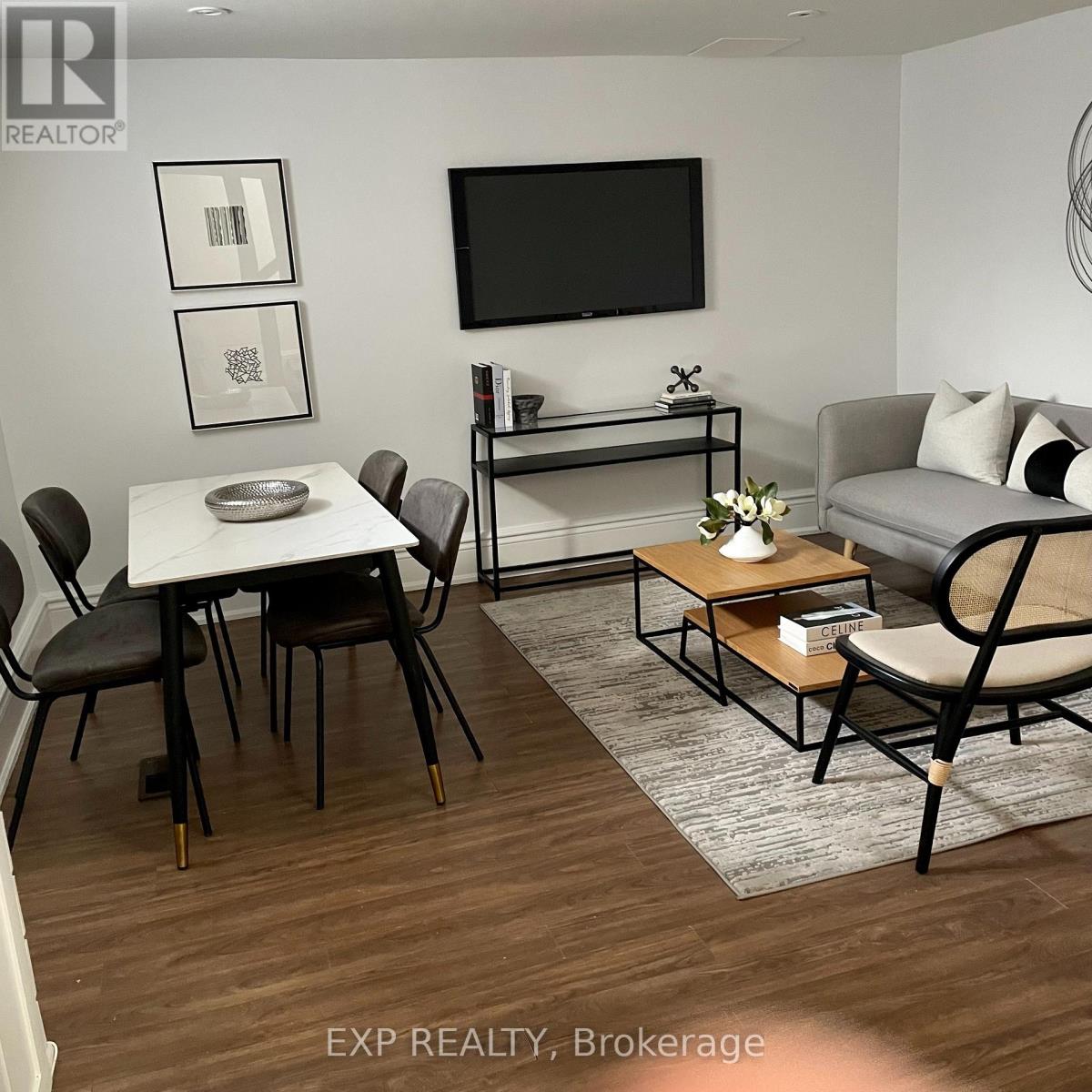 A living room with a white table and chairs, a grey sofa, and a television mounted on the wall.
