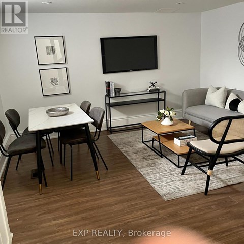 A living room with a white table and chairs, a grey sofa, and a television mounted on the wall.