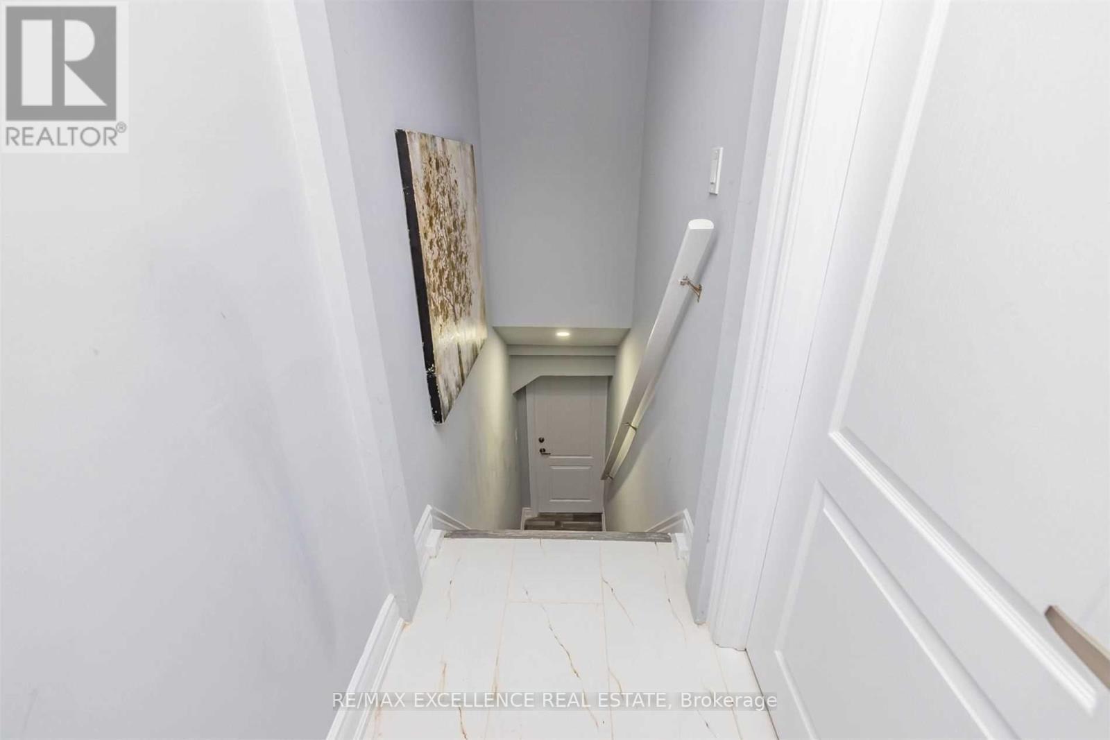 A white hallway with a painting on the wall and a staircase.
