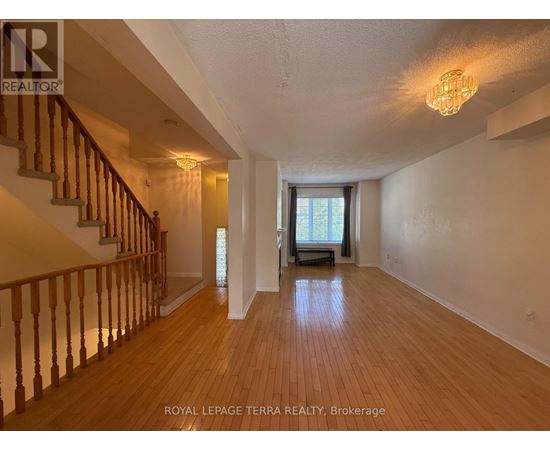 A spacious room with wooden floors and a staircase with wooden railings.