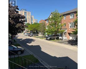 A residential street with cars parked on the side and apartment buildings in the background.