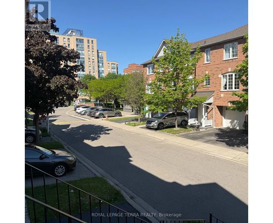 A residential street with cars parked on the side and apartment buildings in the background.