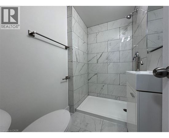 A white toilet sits next to a walk-in shower with a marble tile wall.