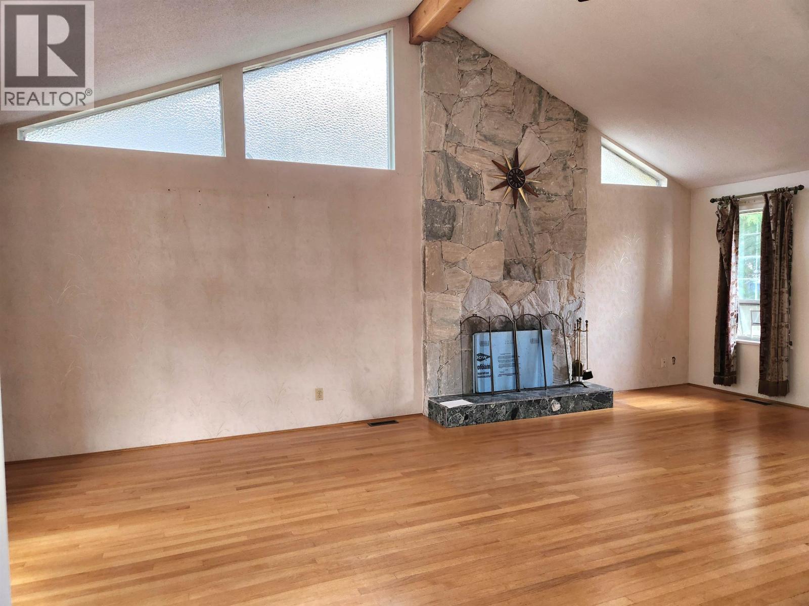 A living room with a stone fireplace and wood flooring.