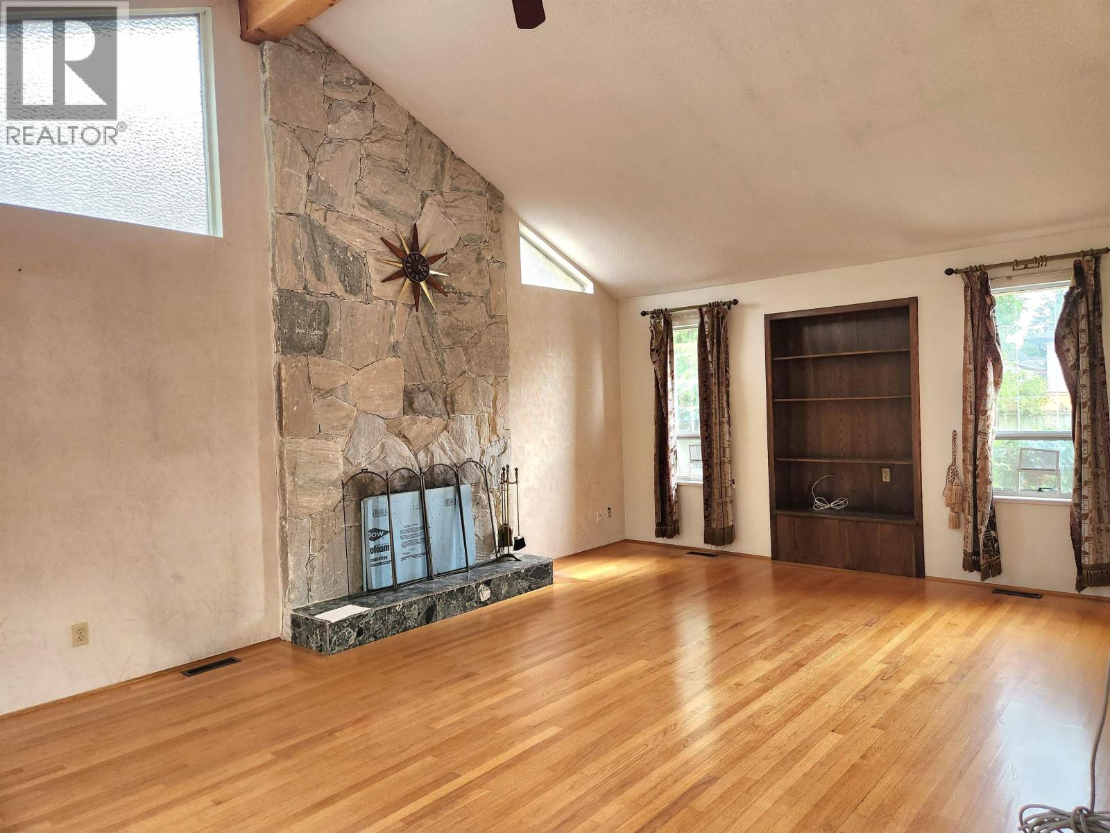 A living room with a stone fireplace and wood flooring.