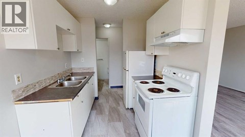 A white kitchen with a stove, sink, and cabinets.