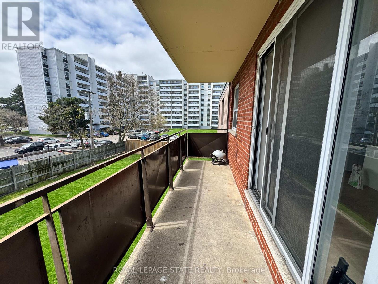 A balcony with a metal railing overlooks a parking lot and apartment buildings.