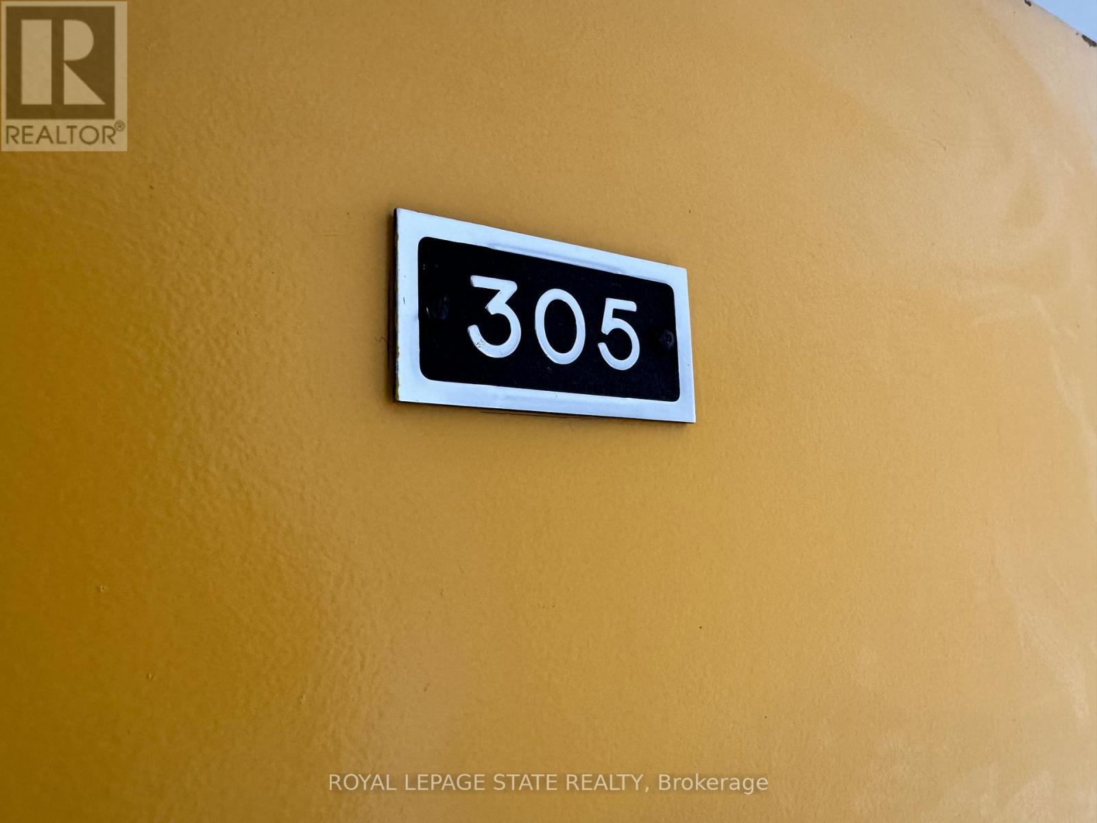 A white sign with the number 305 on it is mounted on a yellow wall.