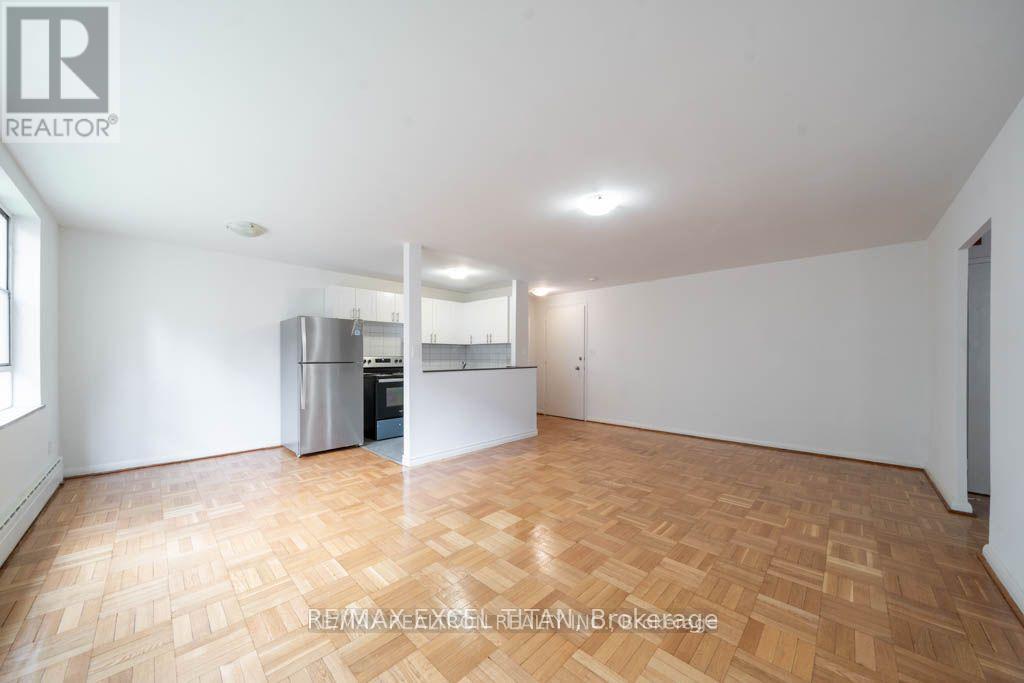 A spacious room with wooden flooring and a kitchen area in the background.