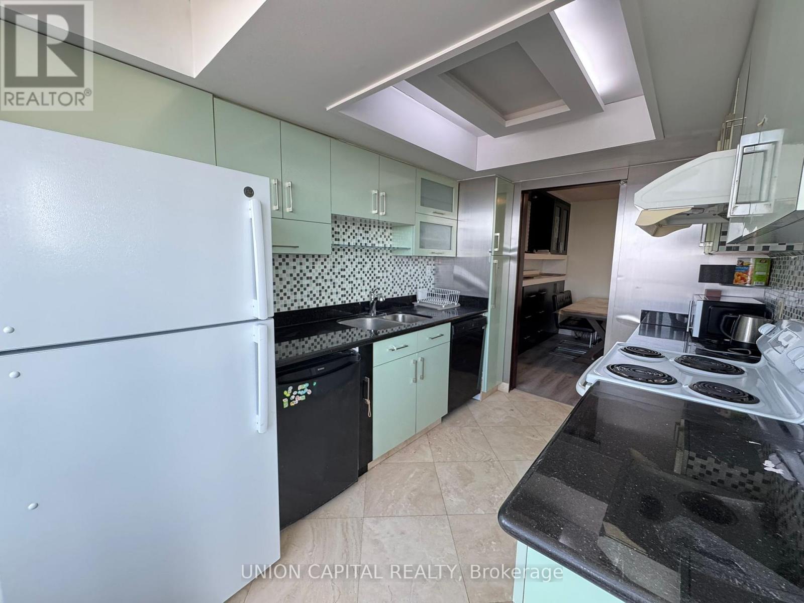 A kitchen with a white fridge and black countertops.