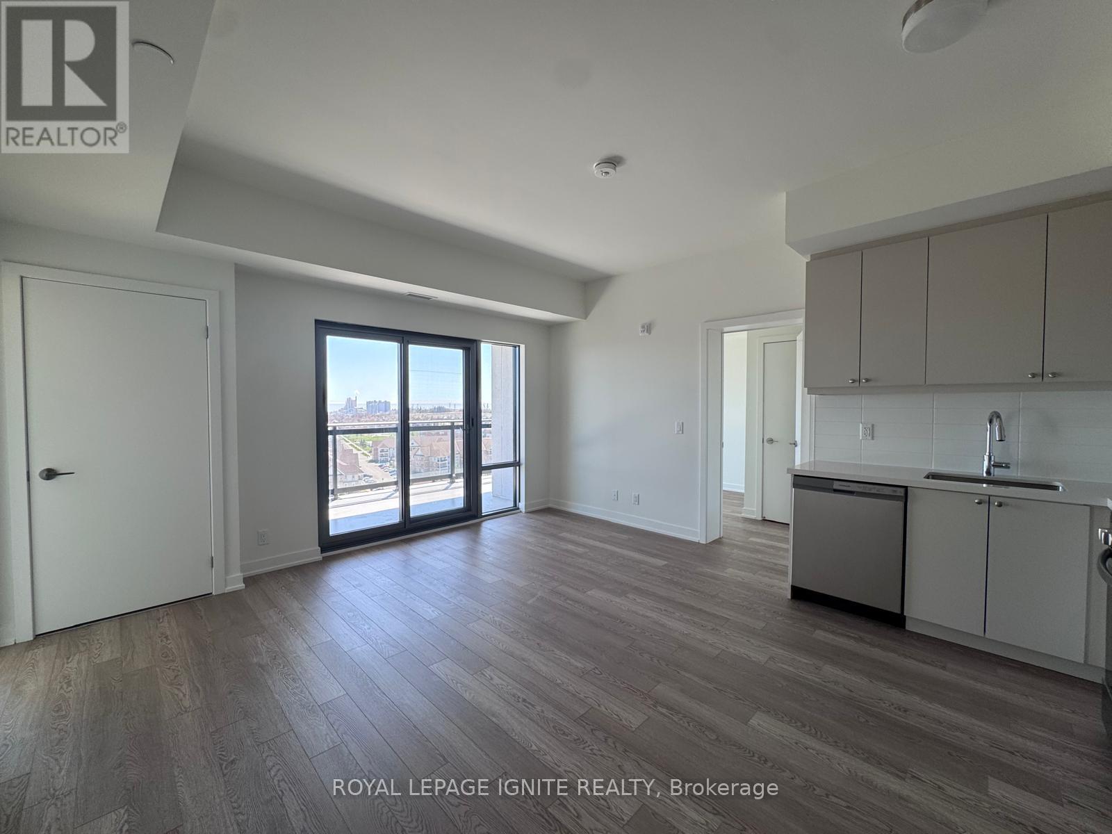 A spacious room with wooden flooring and a kitchen area with white cabinets.