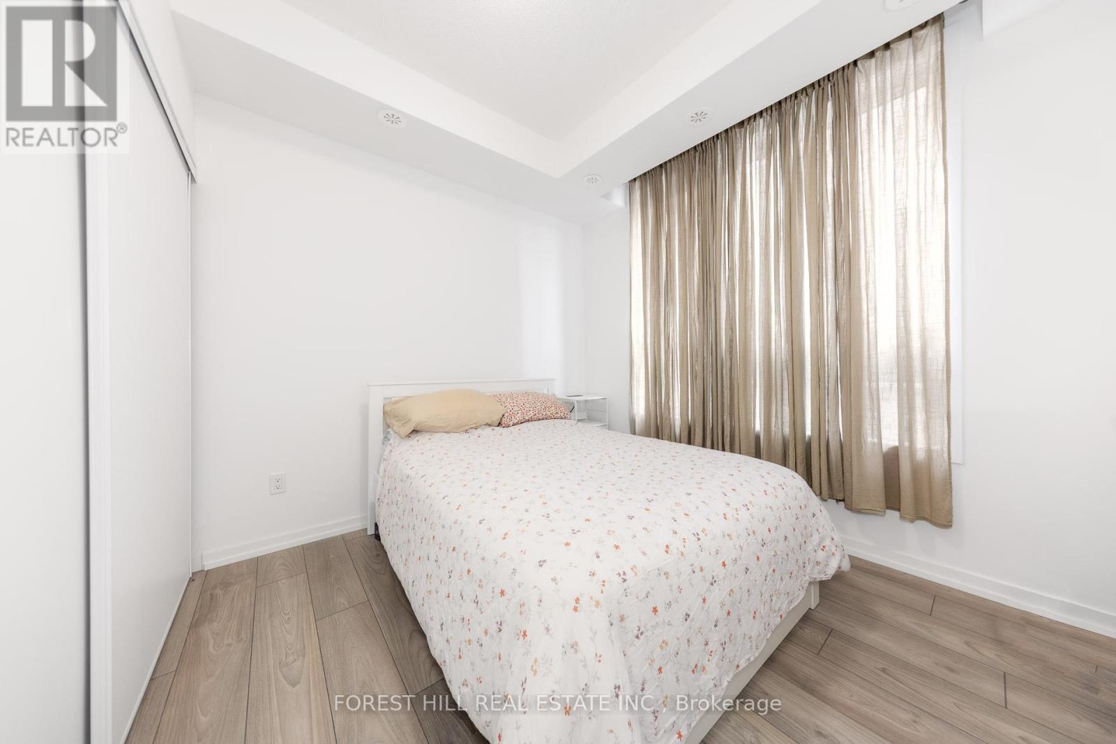 A bedroom with a bed, wooden floors, and a window with curtains.