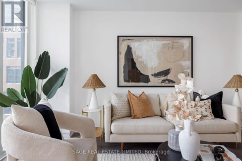 A living room with a white couch, a chair, a table with a vase and a lamp, and a painting on the wall.