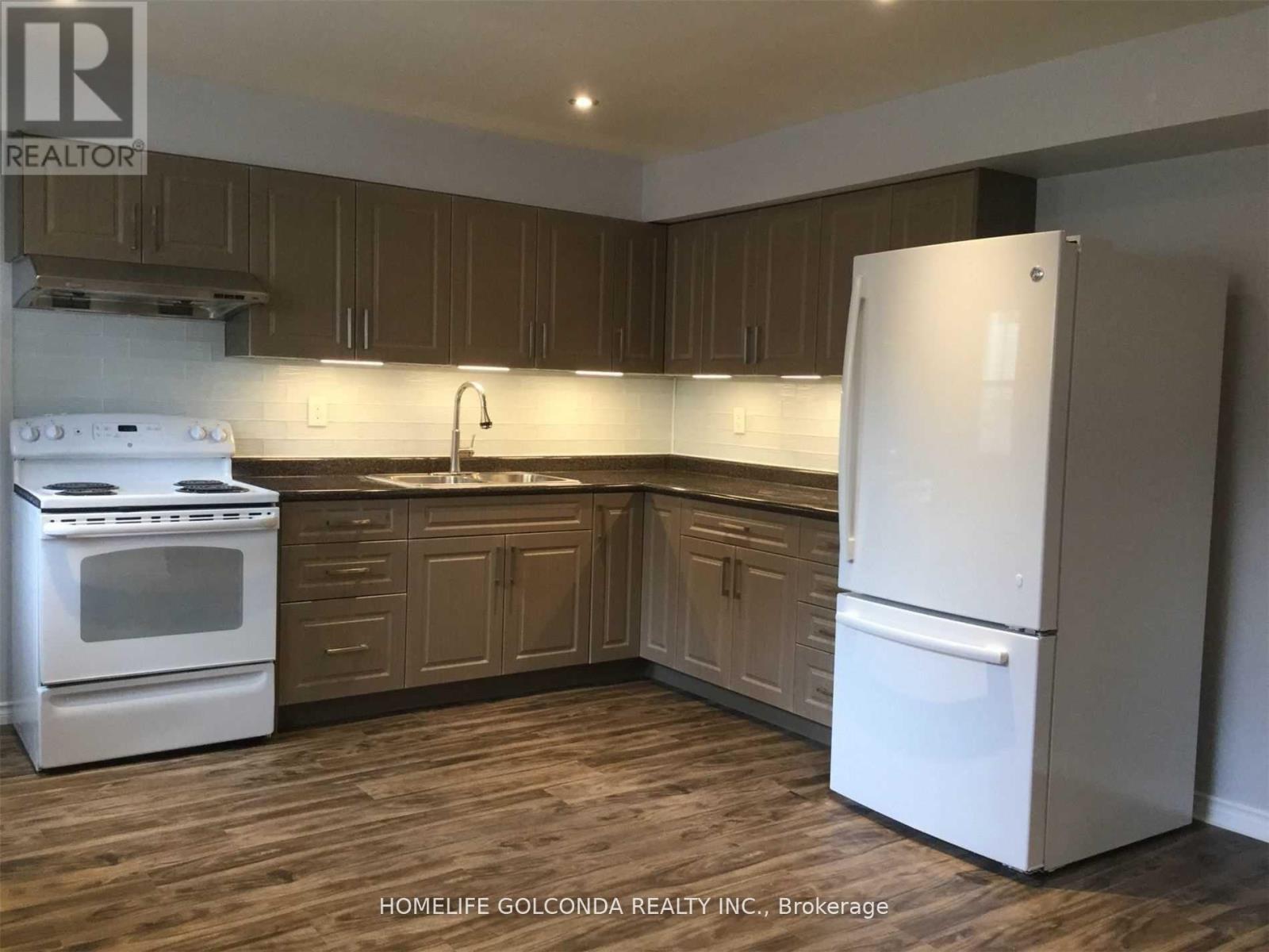 A white refrigerator stands in a kitchen with wooden cabinets and a white stove.