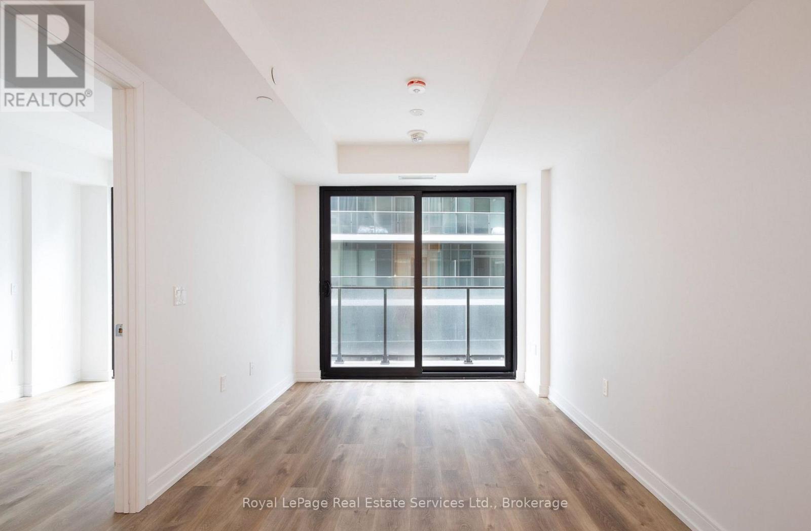 A spacious room with a large window and wooden flooring.