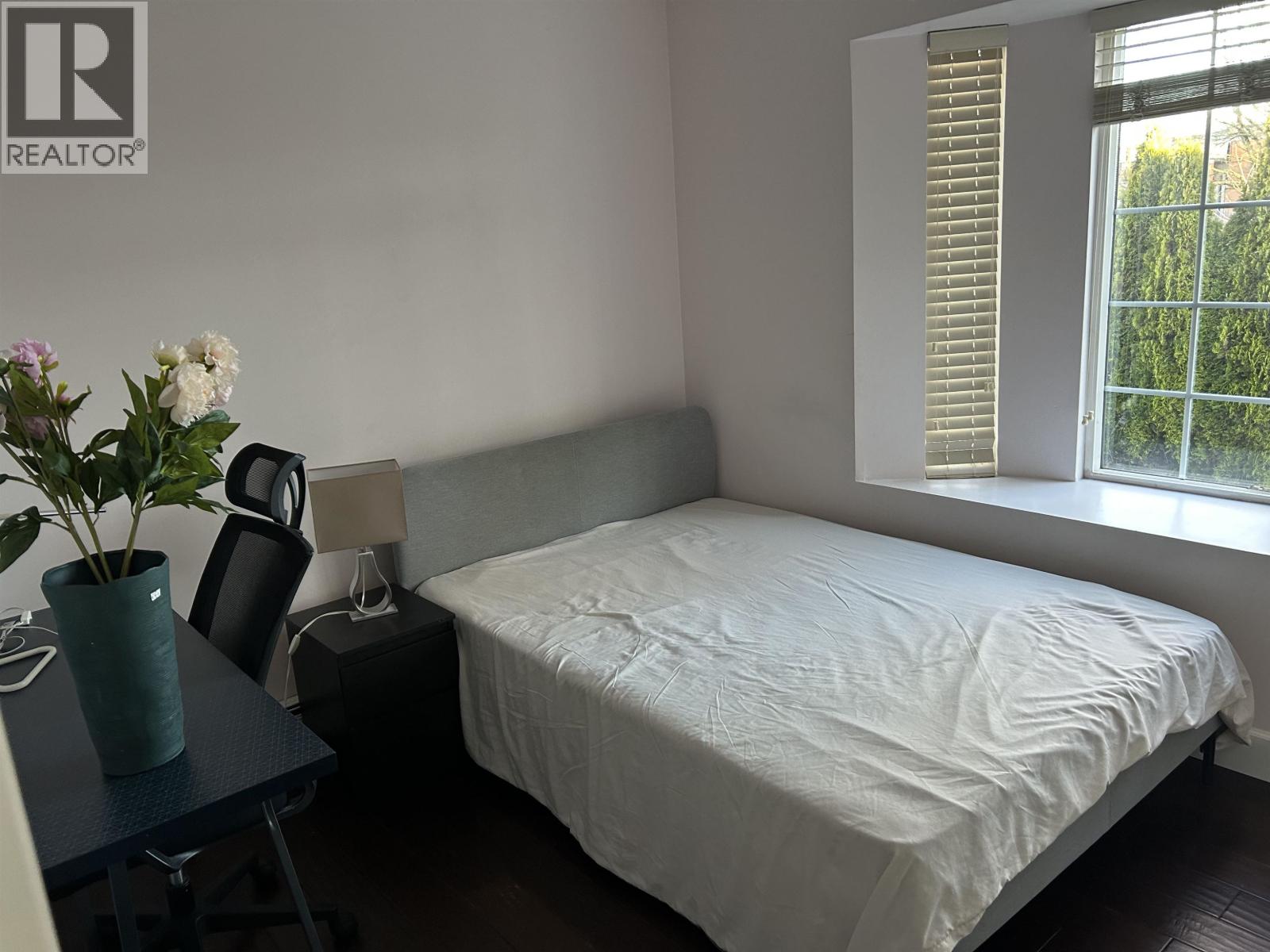 A bedroom with a bed, a table with a vase of flowers, and a window with blinds.