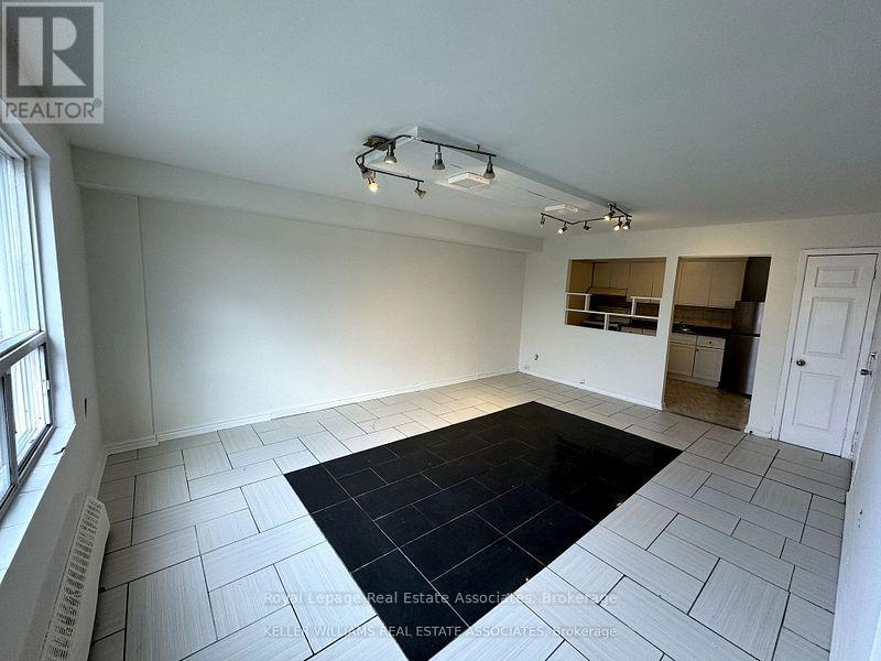 A spacious room with a black rug in the center and a window on the left.