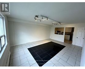 A spacious room with a black rug in the center and a window on the left.