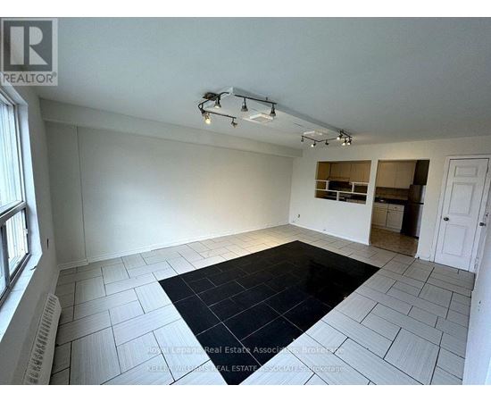 A spacious room with a black rug in the center and a window on the left.