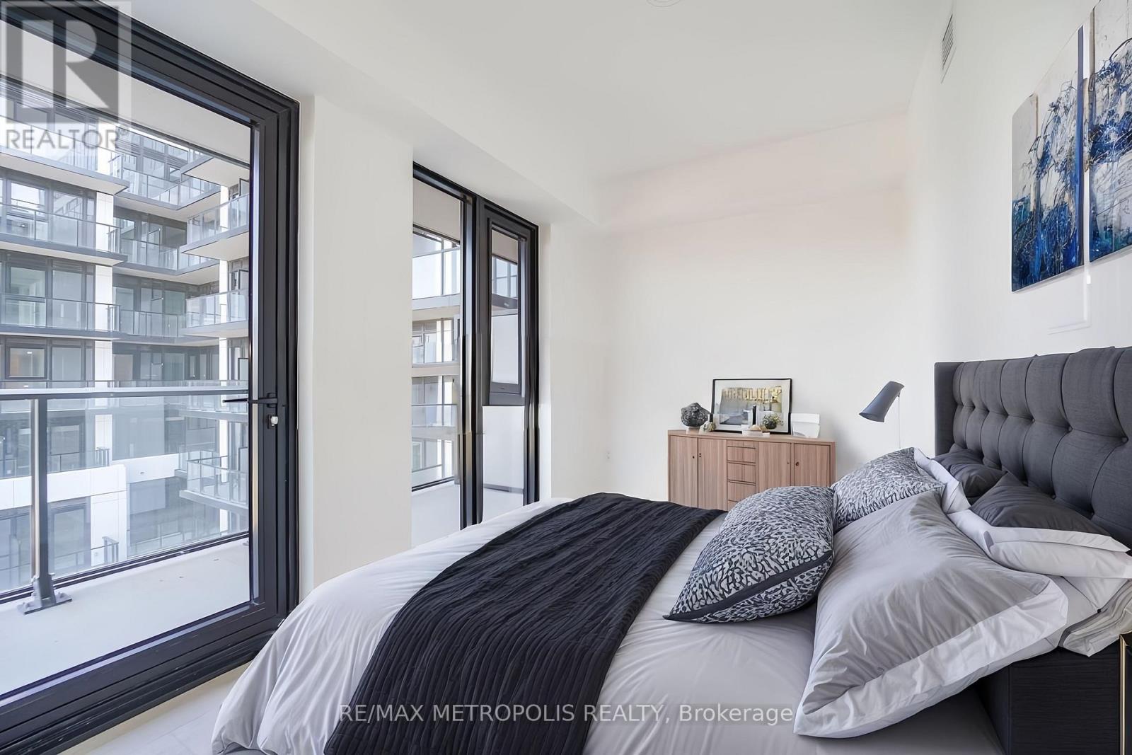 A bedroom with a large bed and a view of a building outside the window.