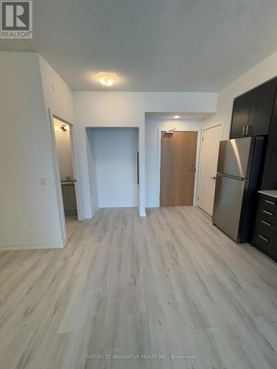 A spacious room with wooden flooring and a refrigerator on the right side.