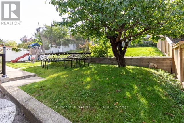 A tree in a yard with a playground in the background.