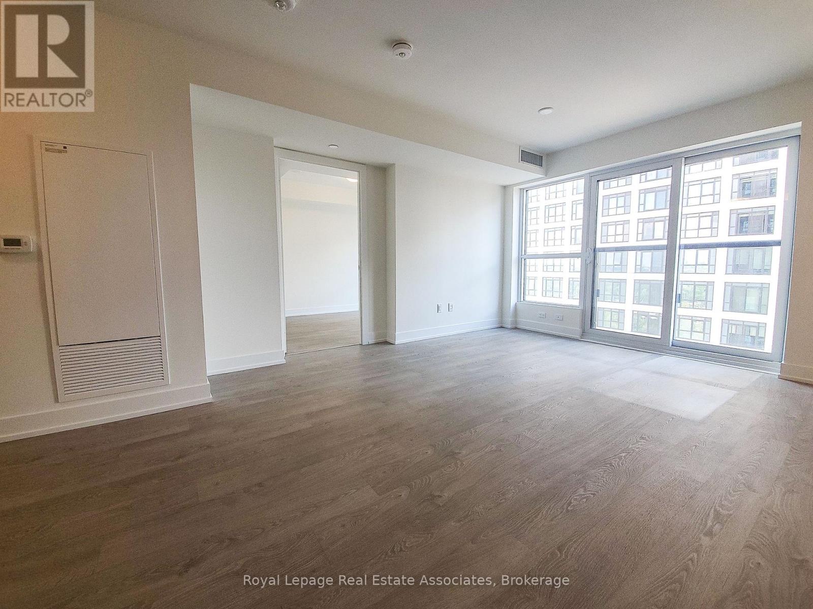 A spacious room with wooden flooring and large windows.