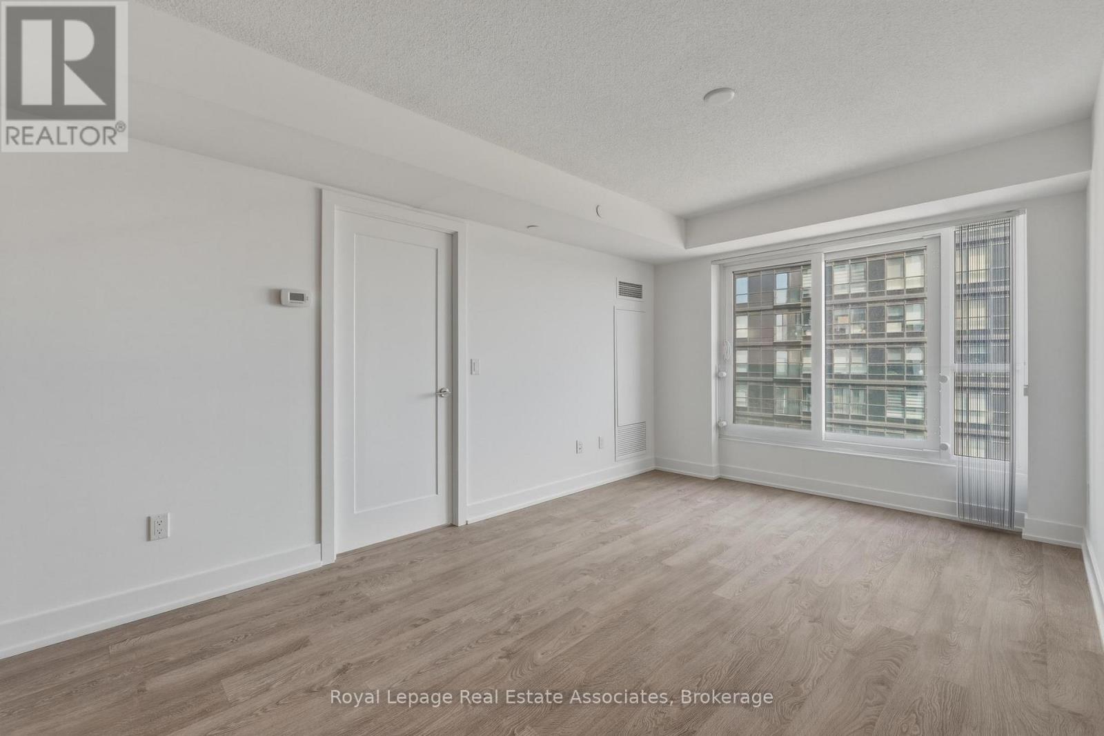 A spacious room with wooden flooring and a large window with a view of a cityscape.