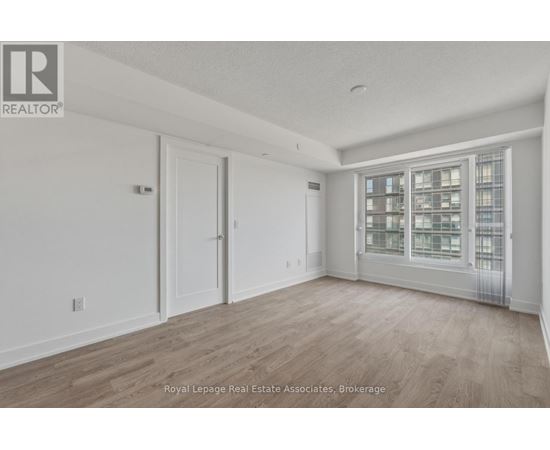 A spacious room with wooden flooring and a large window with a view of a cityscape.