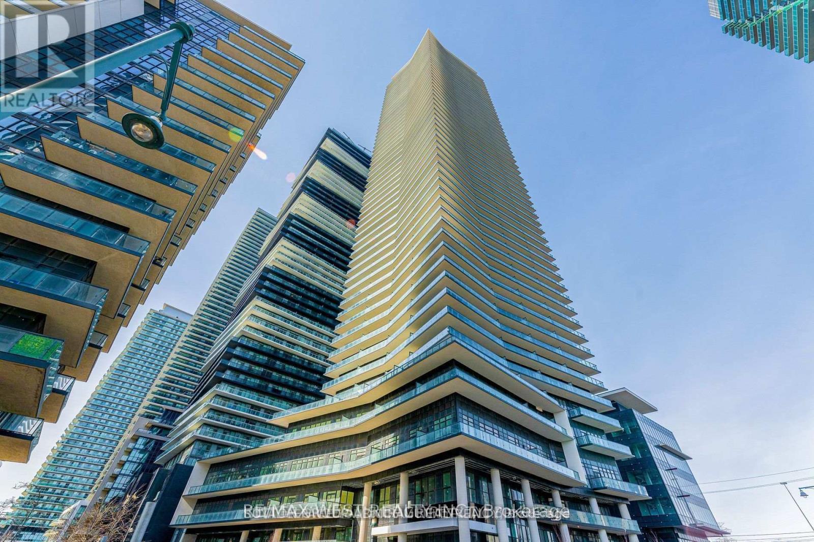 A tall building with a unique triangular top stands next to a shorter building with a blue tinted facade.