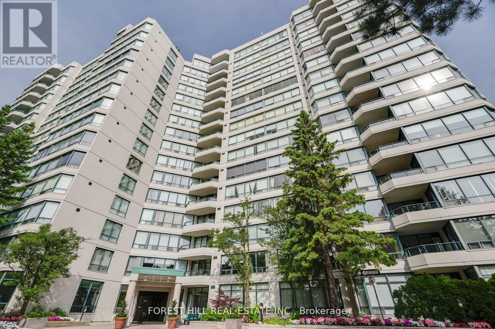 A tall residential building with balconies and trees in front.