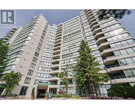 A tall residential building with balconies and trees in front.