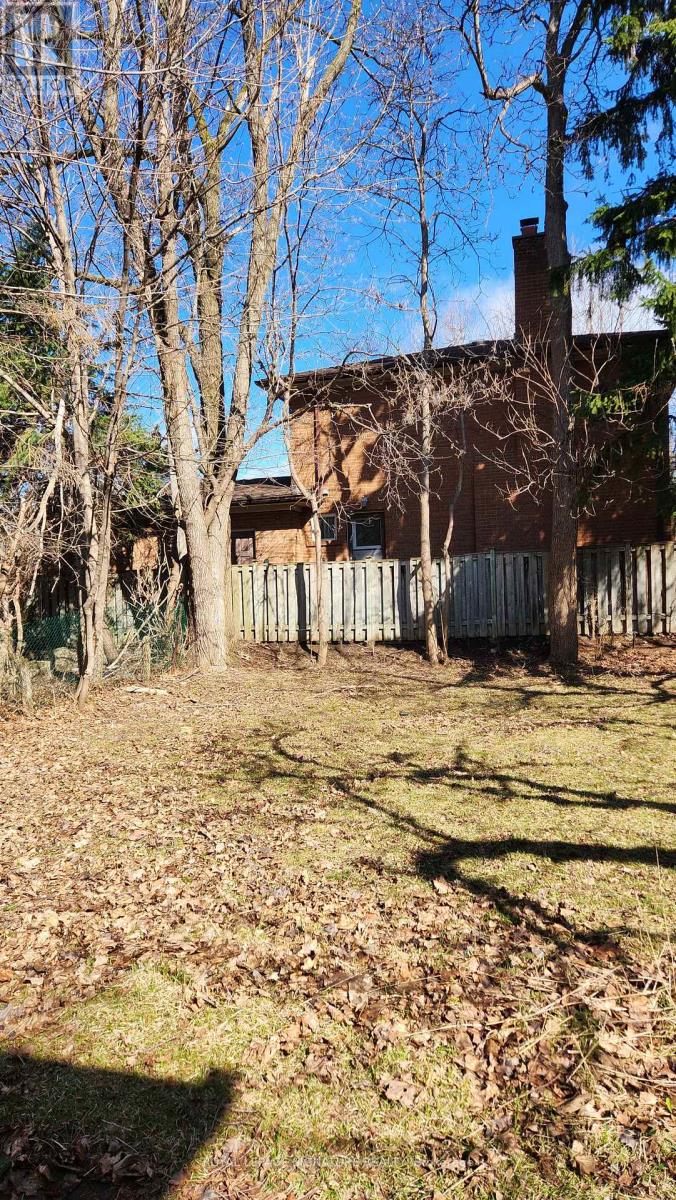 A brown house with a fence and trees in the background.