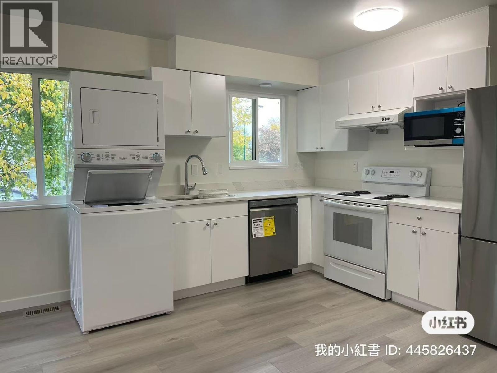 A kitchen with white appliances and cabinets, a window, and a wooden floor.