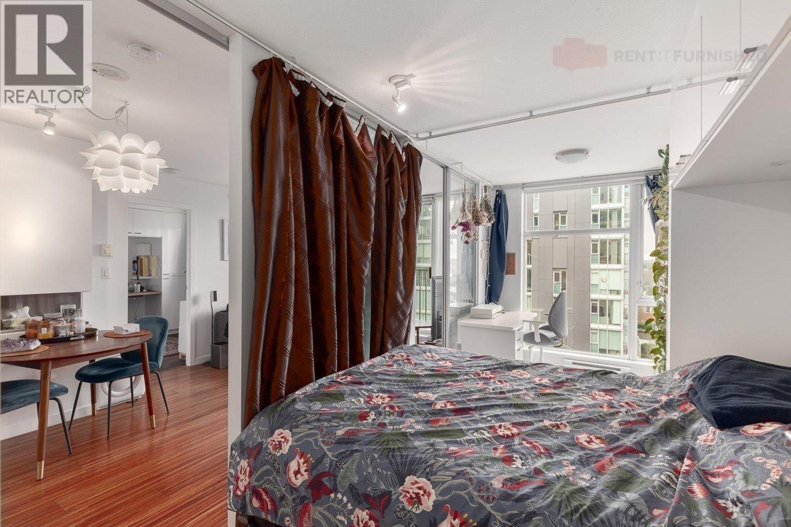 A bedroom with a large bed and a dining area in the background.