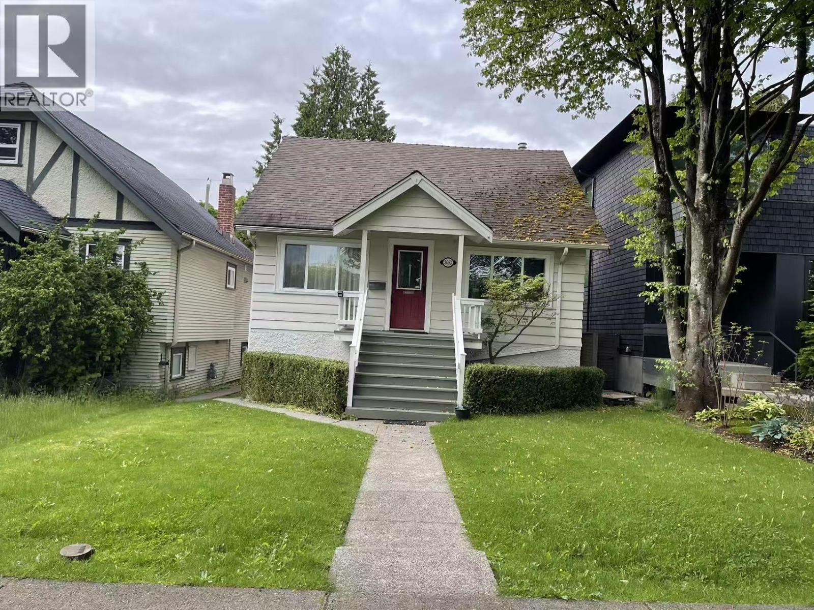 A house with a red door is surrounded by a green lawn.