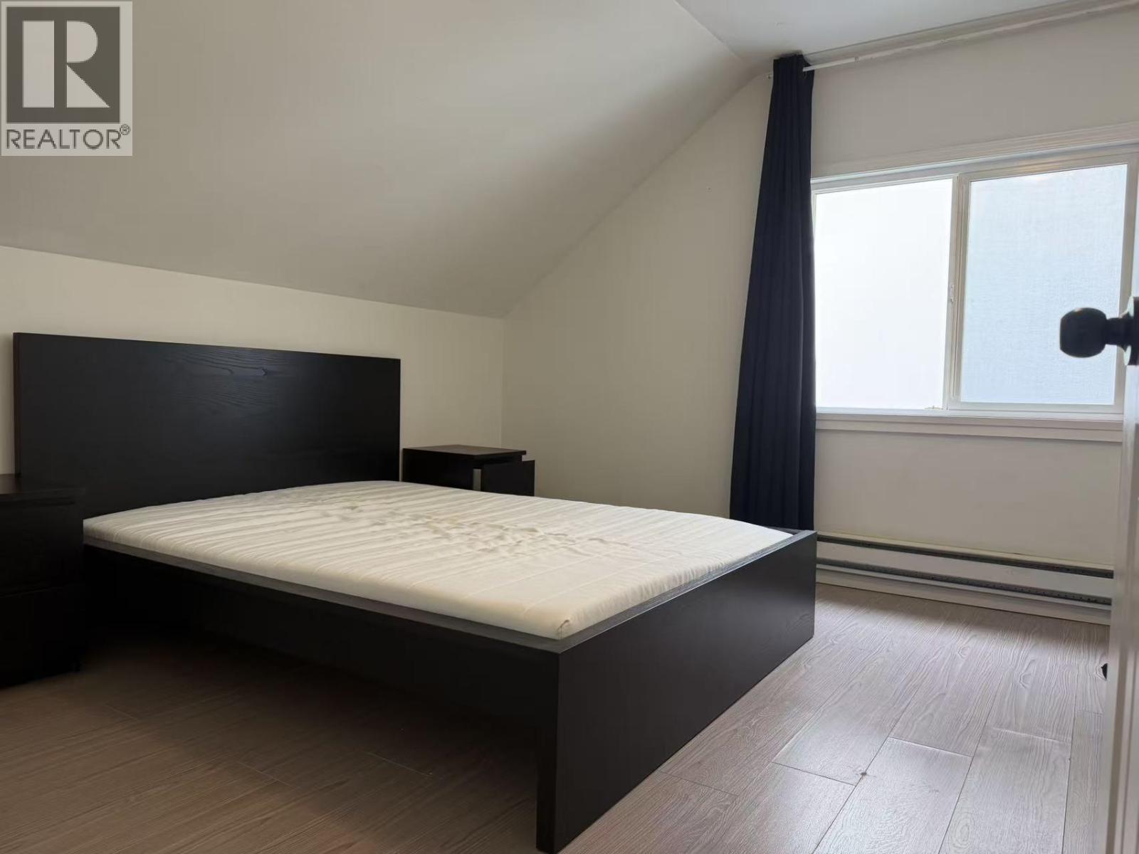A bedroom with a large bed and a window with curtains.