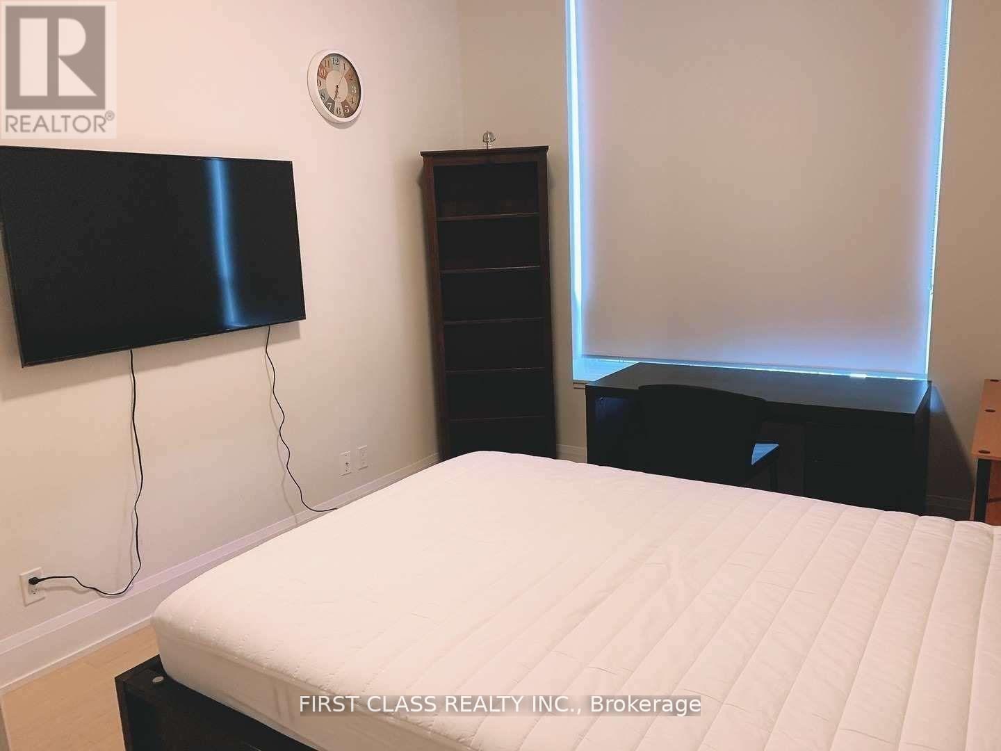 A bedroom with a bed, a television, and a clock on the wall.