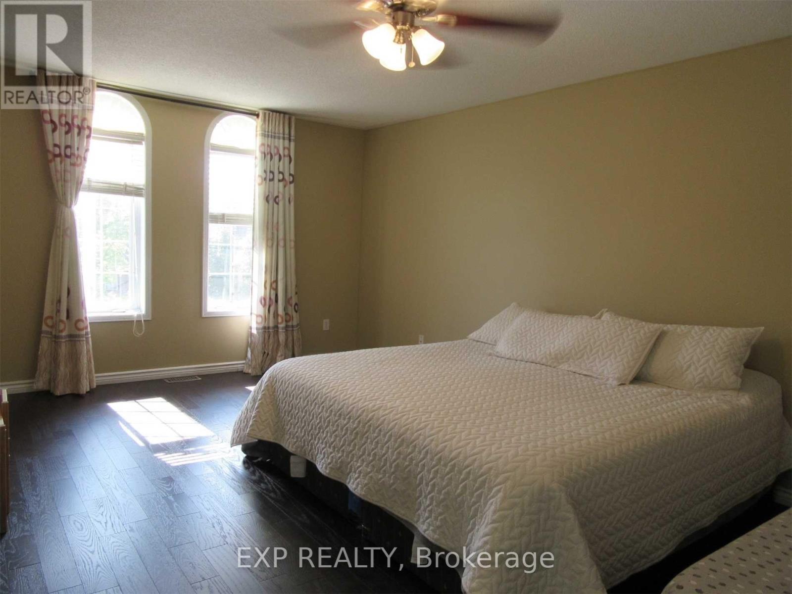 A bedroom with a bed, a ceiling fan, and two windows.
