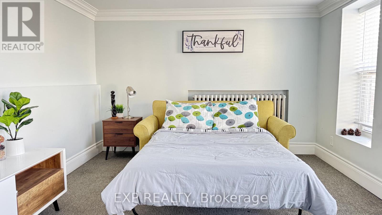 A bedroom with a bed, a yellow chair, and a plant.