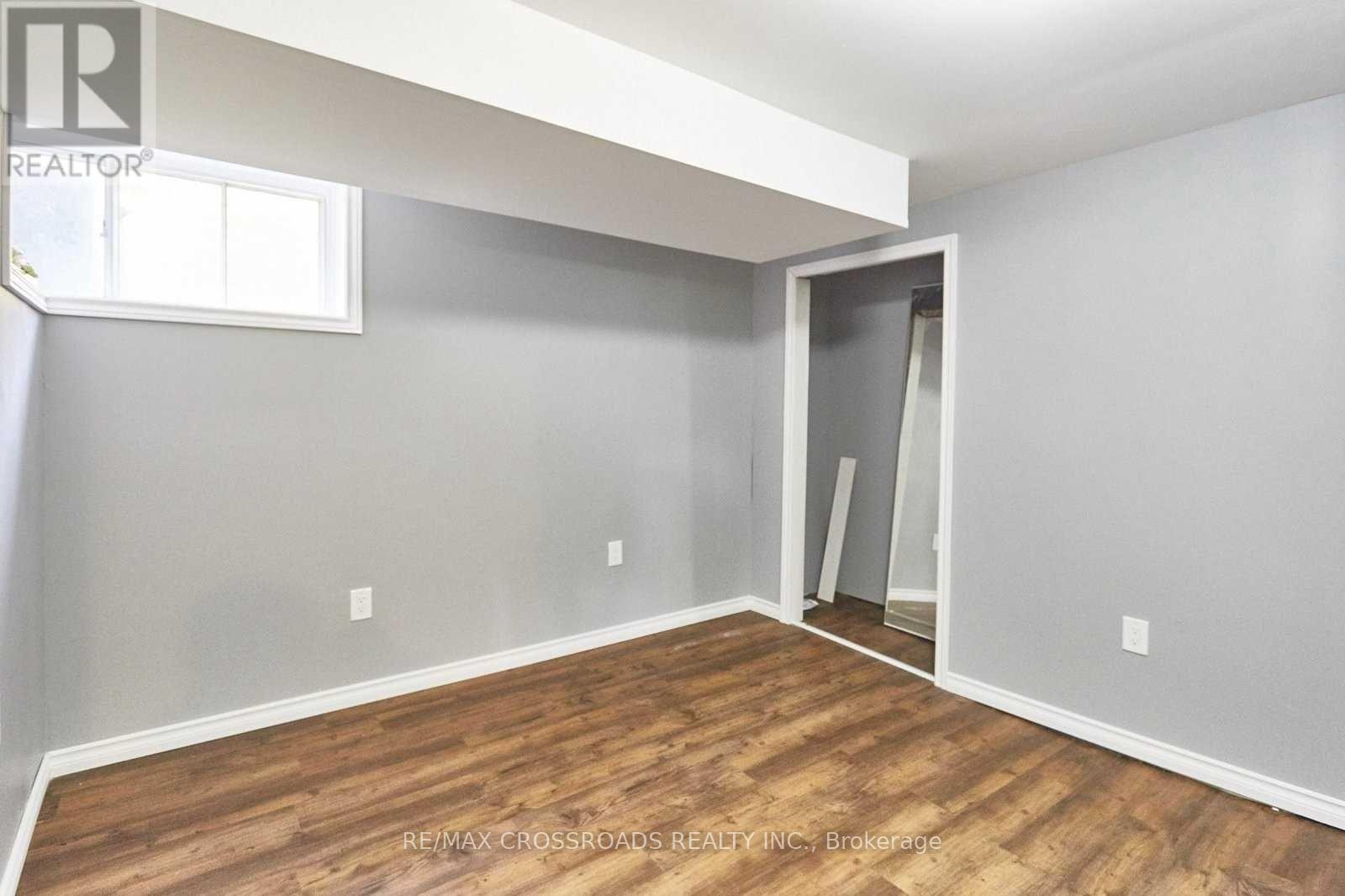 A room with a wooden floor and a grey wall with a window.