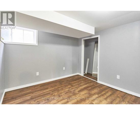 A room with a wooden floor and a grey wall with a window.