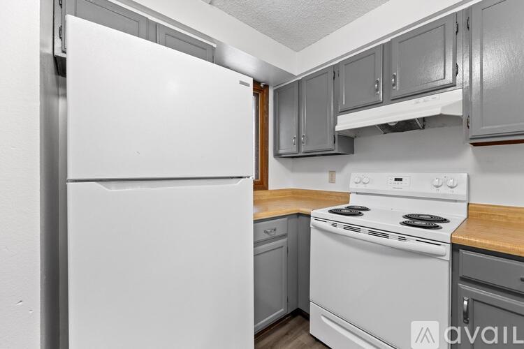 A white refrigerator stands in a kitchen with a stove and cabinets.