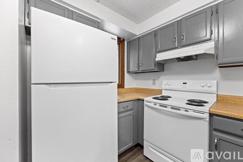 A white refrigerator stands in a kitchen with a stove and cabinets.