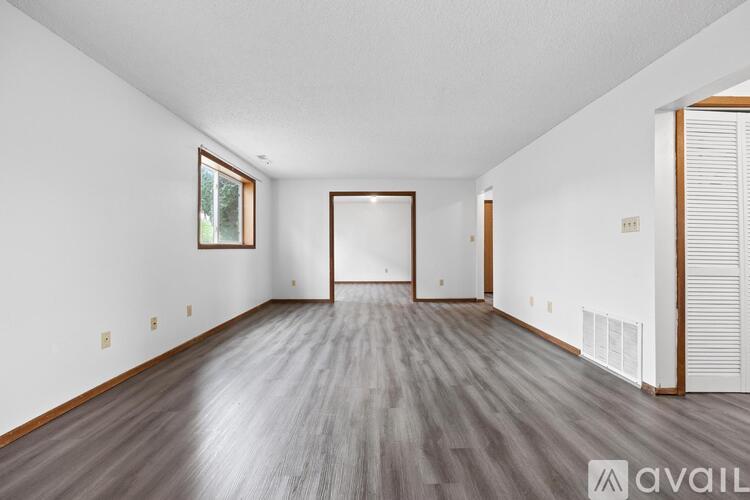 A spacious room with wood flooring and a large window.